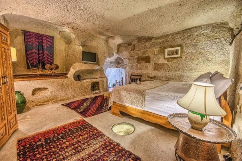 A rustic bedroom with a stone wall, a bed, a wooden cabinet, a television, and a lamp. 5