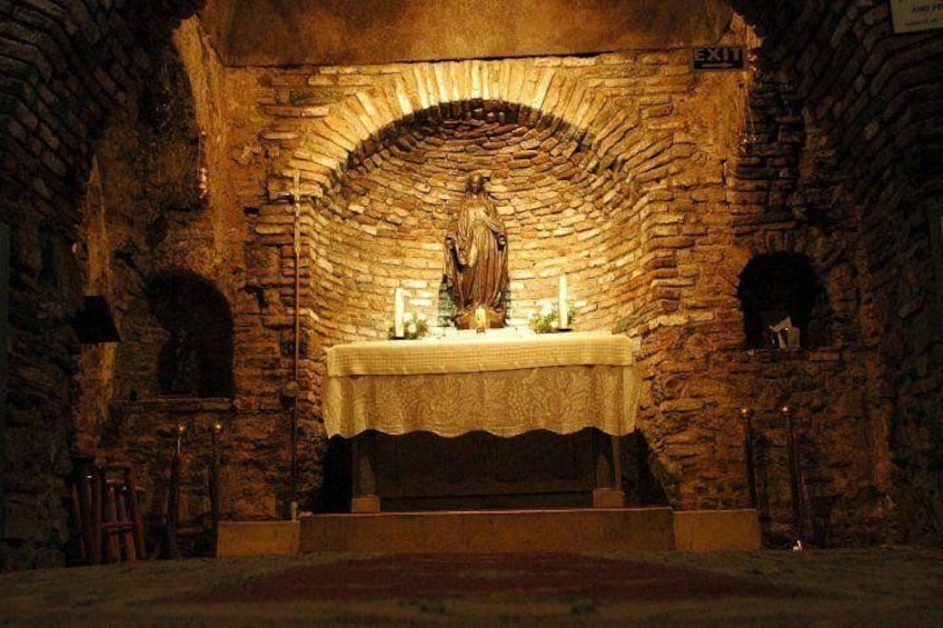 An arched stone structure with a statue on a table, a candle, and a sign indicating an exit. 3