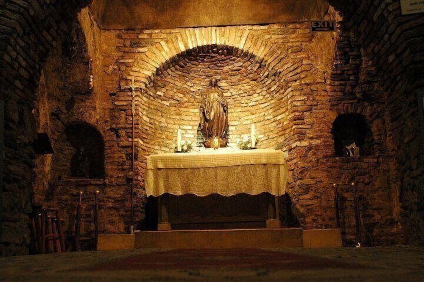 A stone chapel with a statue on an altar, arched brick walls, and a lit candle. 3