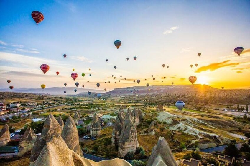 A landscape with numerous hot air balloons, rocky formations, and a sunset. 1