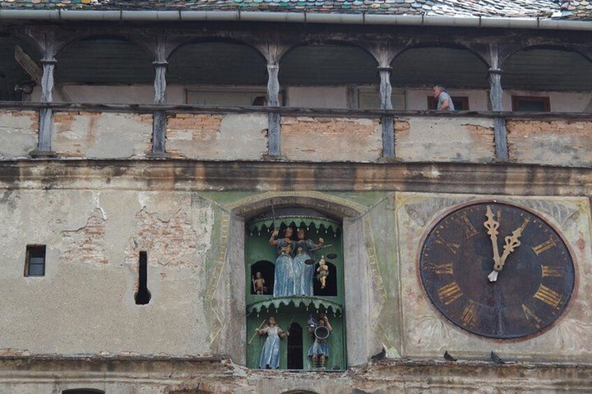 La façade d’un bâtiment usée par le temps, ornée d’une grande horloge, d’une porte verte décorée de motifs et d’un balcon où se trouve une personne. 4