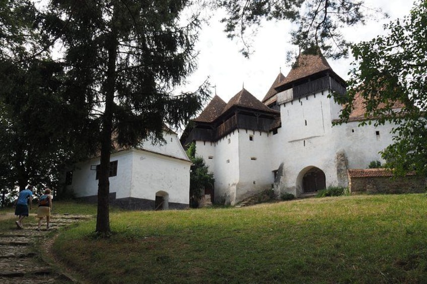 A historic castle with white walls and dark roofs, surrounded by a grassy area and a few people walking nearby. 2