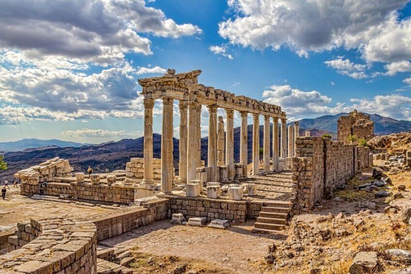 Ancient ruins with columns, a stone staircase, and a mountainous backdrop. 1