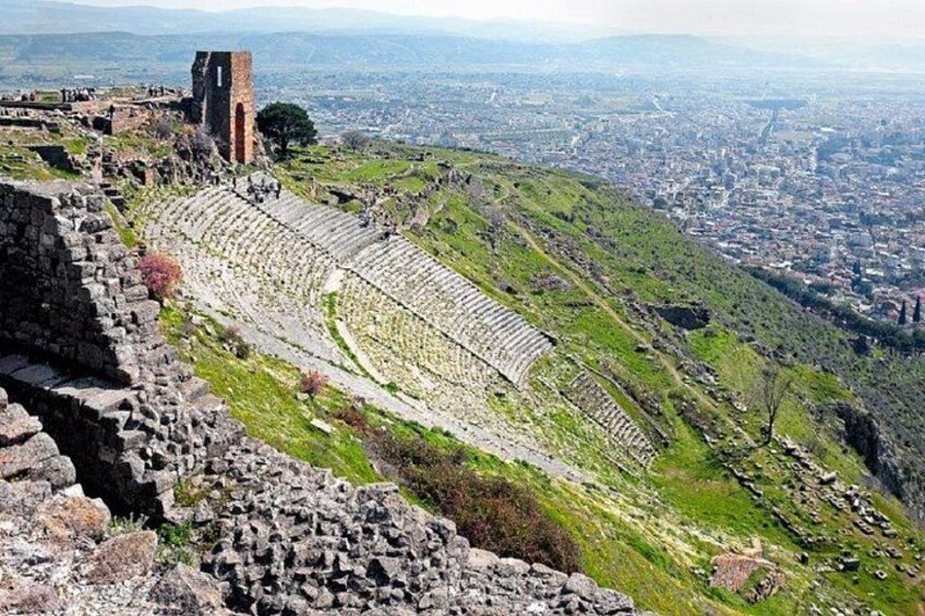 An ancient amphitheater with stone seating and a tower on a hill overlooking a city. 3