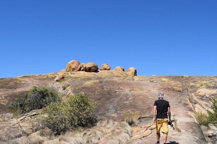 A person hiking on a rocky trail with large boulders and sparse vegetation. 4