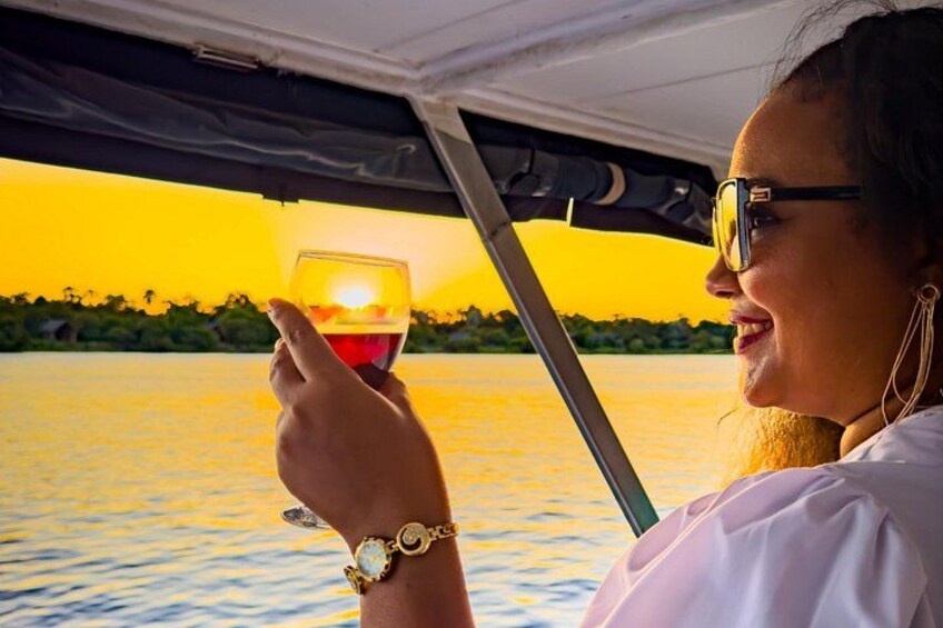 A person holding a glass of red wine, wearing a white shirt, and a watch, with a sunset over water. 4