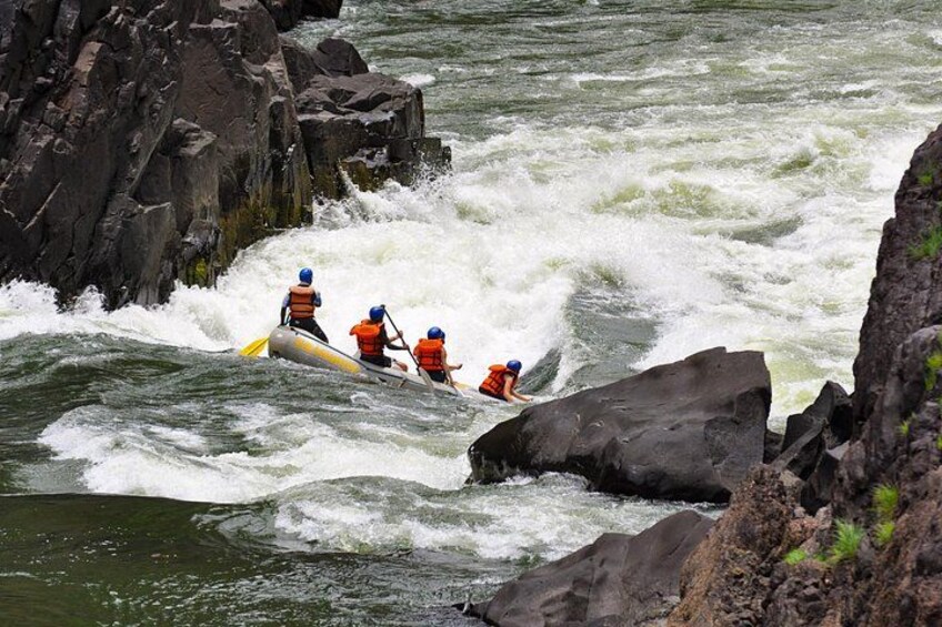 Un groupe de personnes à bord d’un radeau navigue sur une rivière à courant rapide, entourée d’un paysage rocheux. 2