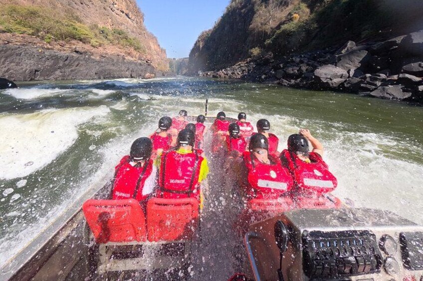 Un grupo de personas con chalecos salvavidas rojos en una embarcación navegando un río con rápidos. 3