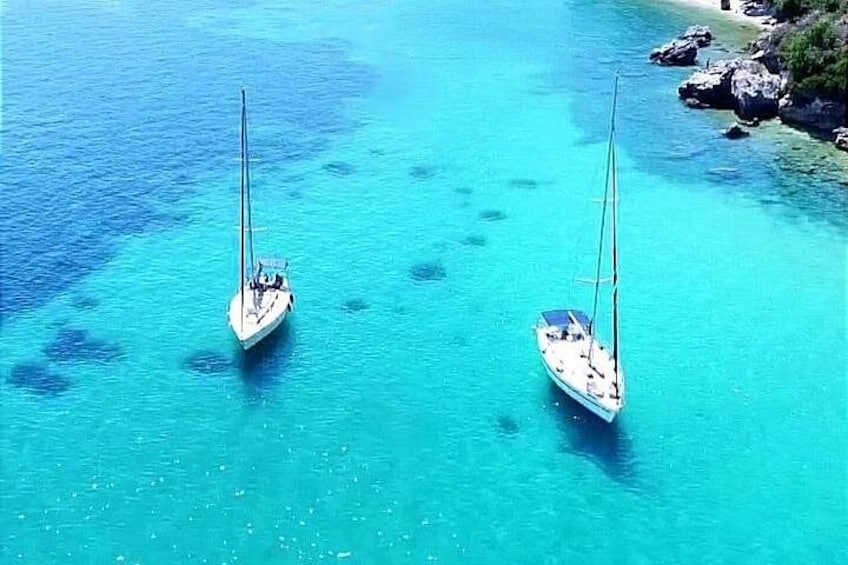 Two sailboats on turquoise water with a rocky shoreline in the background. 1