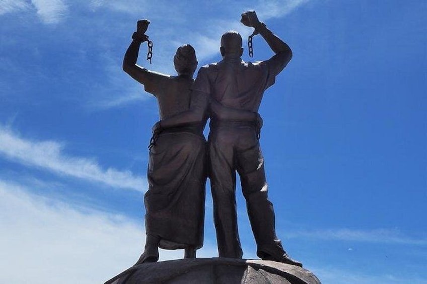 Una statua raffigura due figure che stringono catene, sullo sfondo un cielo azzurro limpido. 3