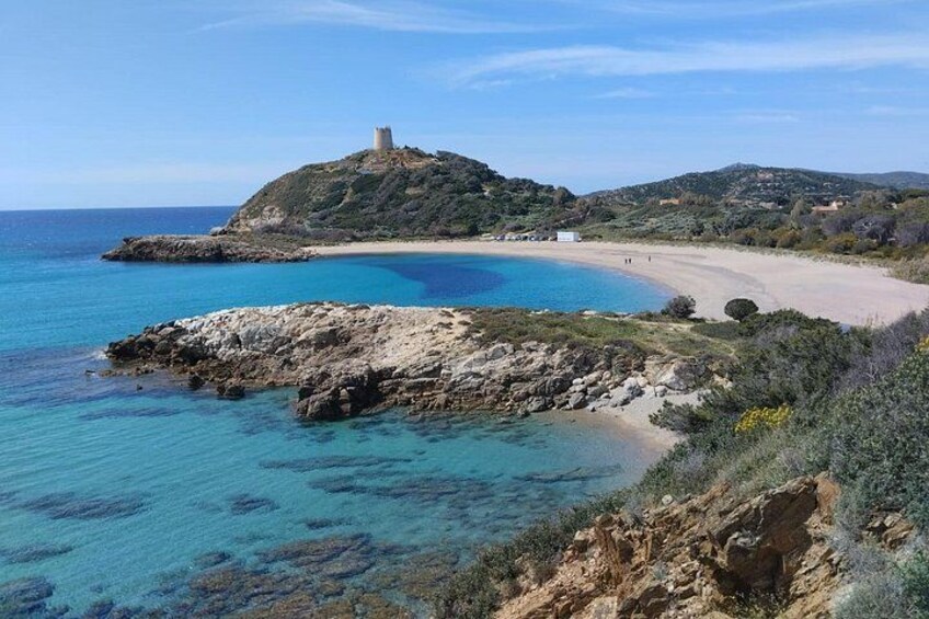 A coastal landscape with a beach, rocky outcrops, and a hill with a structure on top. 1
