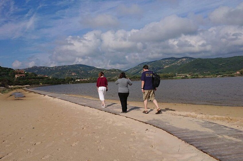 Three people walking along a concrete path by a body of water with mountains in the background. 2