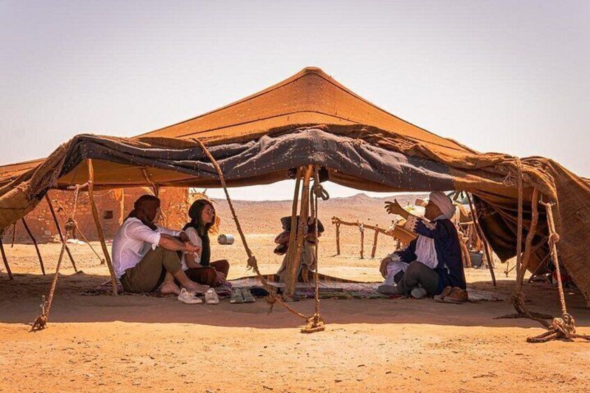 A desert campsite with tents and people sitting under them. 1