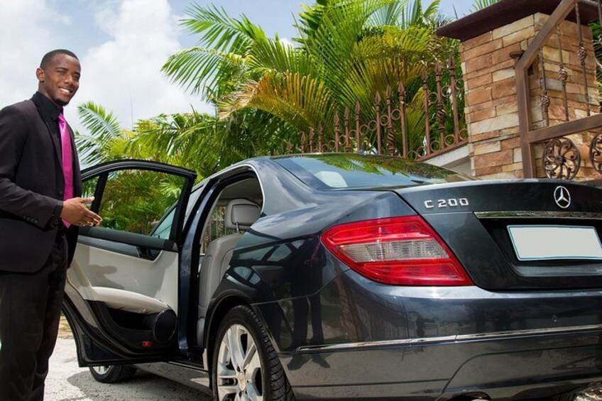 Un homme en costume se tient à côté d’une Mercedes-Benz C200 noire, la portière ouverte. 2