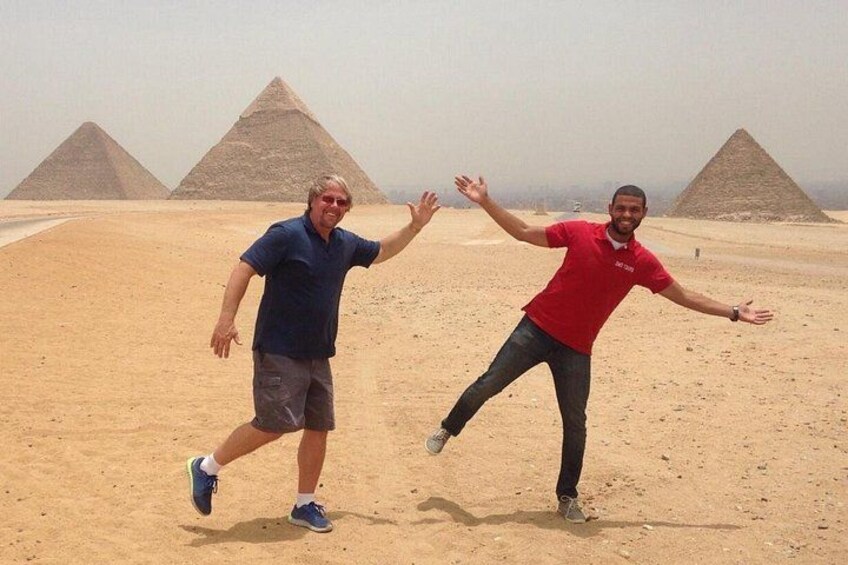 Two people in a desert with pyramids in the background. 1