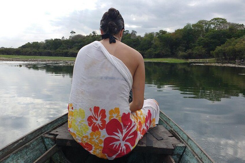 A person sitting on a boat with a floral pattern, surrounded by calm water and greenery. 1