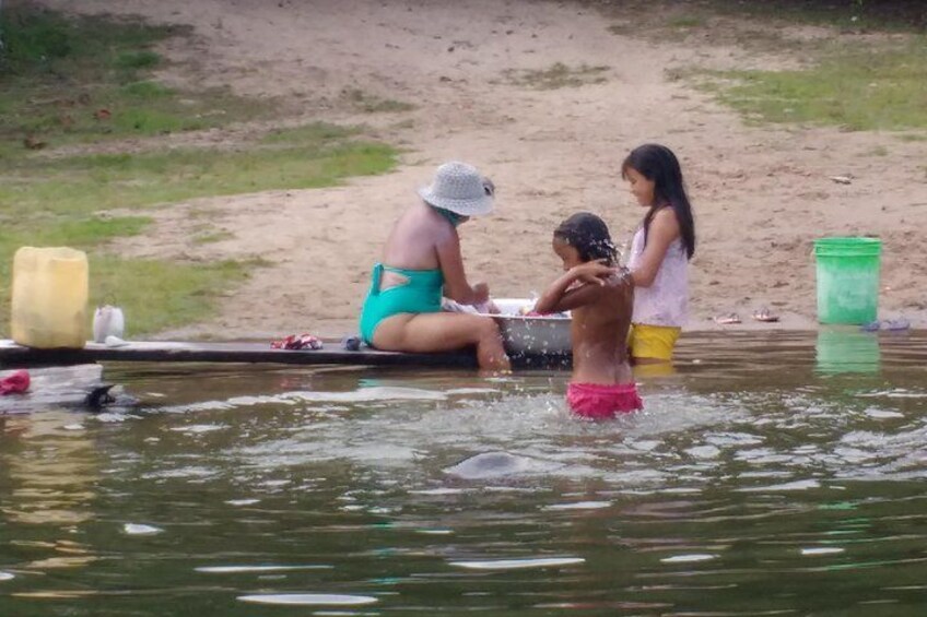 People sitting and standing in a body of water, with a sandy shore in the background. 5