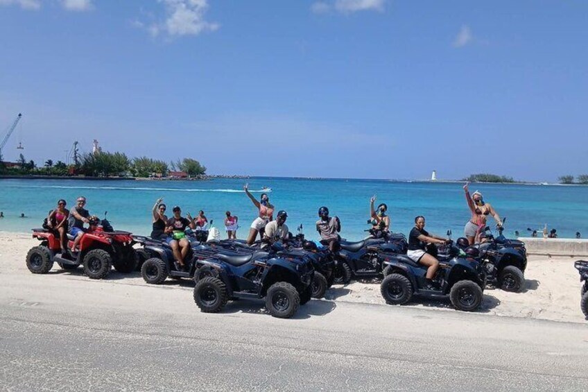 A group of people on ATVs on a beach with the ocean in the background. 1