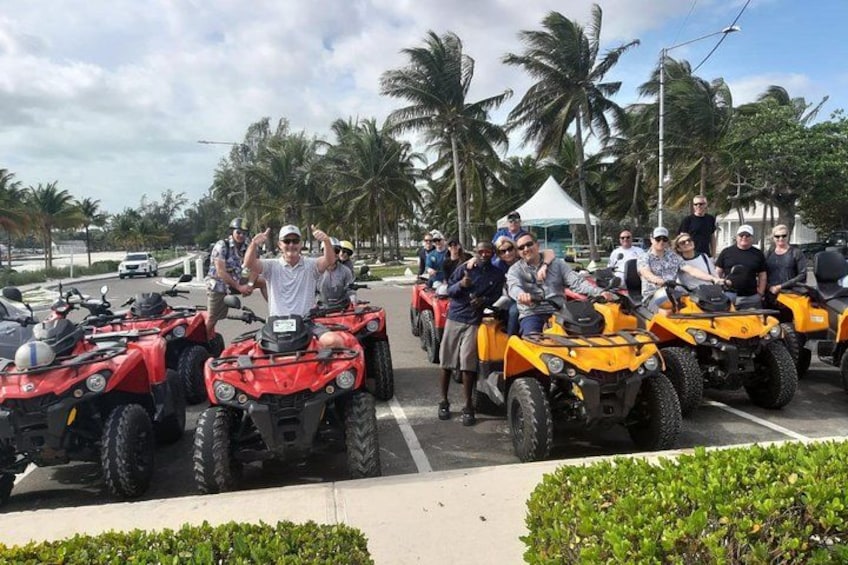 Een groep mensen op quadbikes, geparkeerd op een straat met palmbomen op de achtergrond. 3
