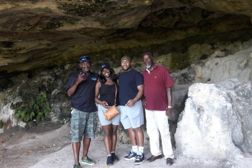 A group of people standing in a cave with rocky walls and a large boulder in the foreground. 2