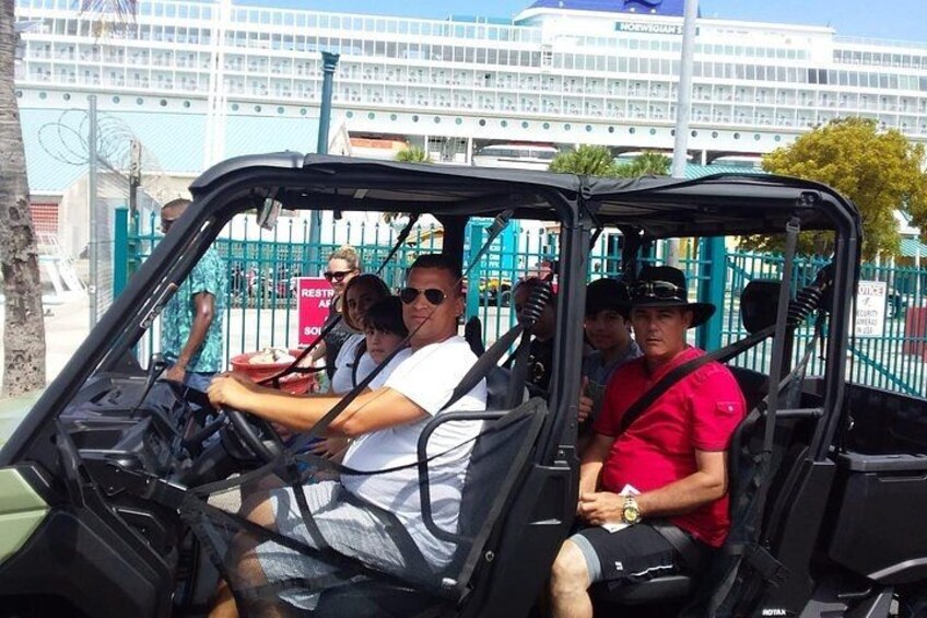 A group of people in a safari vehicle with a building and a fence in the background. 1