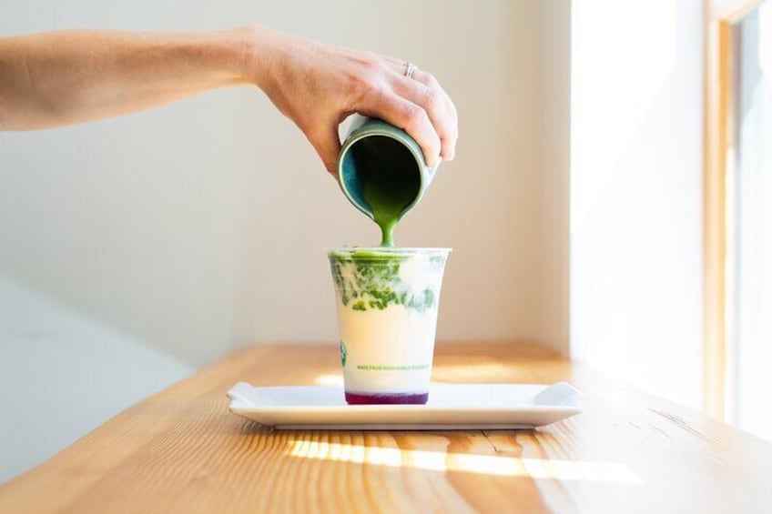 A hand pouring a green liquid into a layered drink in a glass. 2