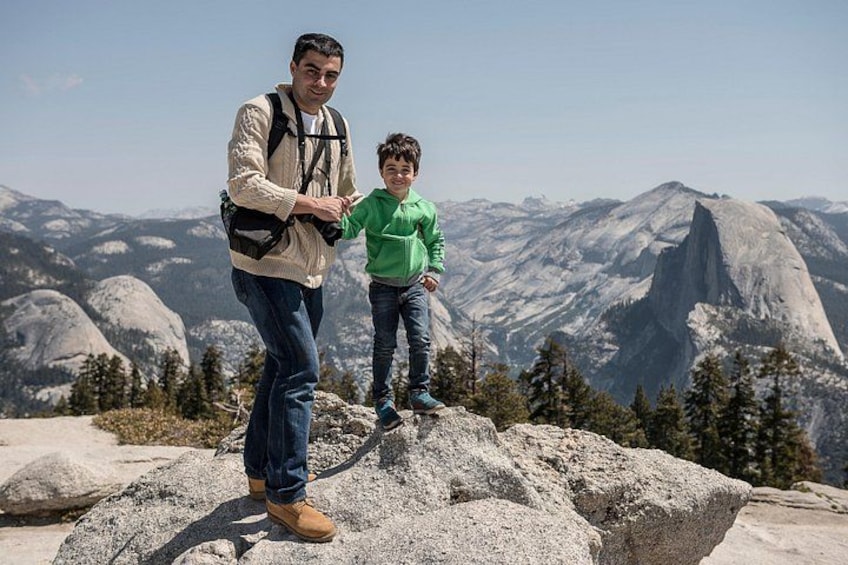 Two people standing on a rocky outcrop with a mountainous landscape in the background. 3