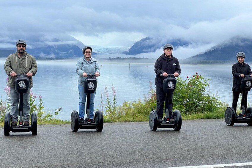 Vier Personen auf Segways am See, im Hintergrund Berge. 1