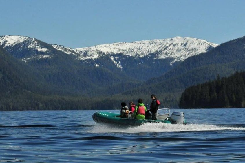 A group of people on a green inflatable boat on a lake with snow-capped mountains in the background. 1