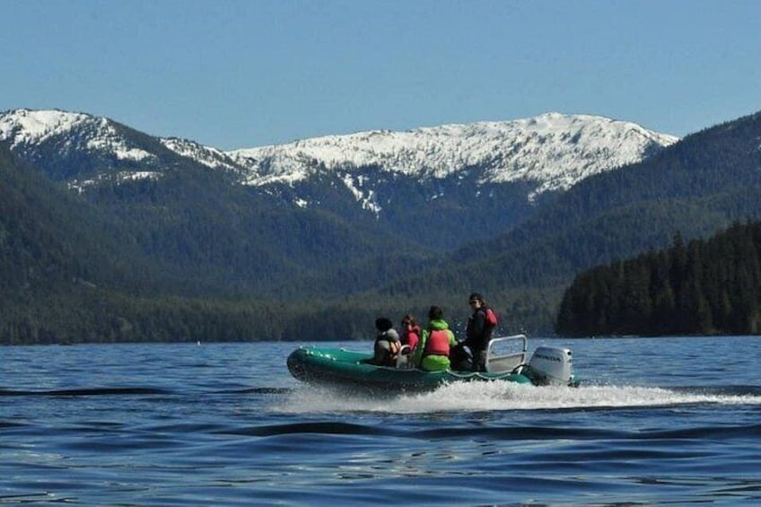 A group of people on a green inflatable boat on a lake with snow-capped mountains in the background. 1