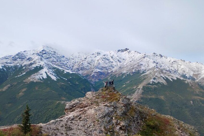A mountain peak with snow-capped summits and a rocky outcrop with two figures standing on it. 2