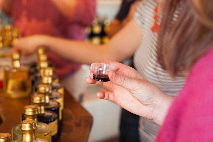 A person holding a small glass of red liquid, likely wine, with a row of bottles in the background. 4