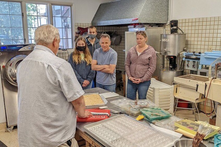 A group of people in a kitchen with a large industrial mixer, a food processor, and various kitchen equipment. 2