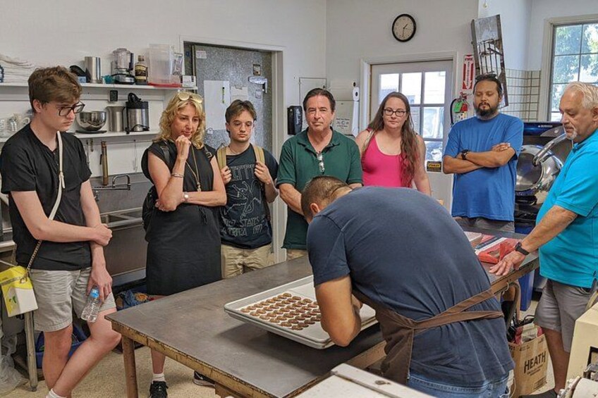 A group of people in a kitchen setting, some standing and some bending over a table with food items. 2