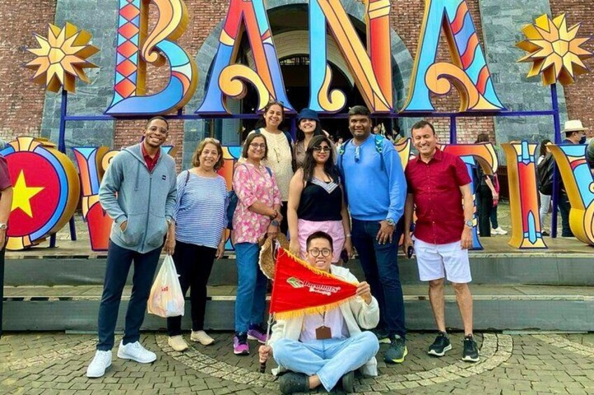 A group of people standing in front of a colorful sign with the letters 'BAN' and 'A' prominently displayed. 2