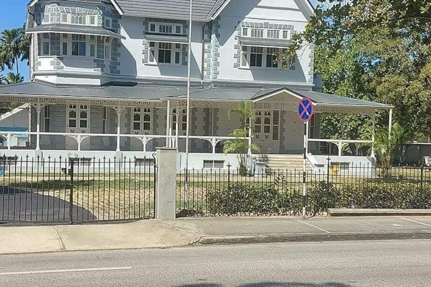 A large, white, two-story building with a balcony and a fence in front. 2