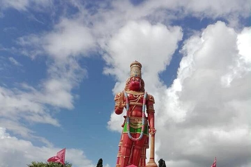 A large red statue of a deity with a green base, set against a partly cloudy sky. 1