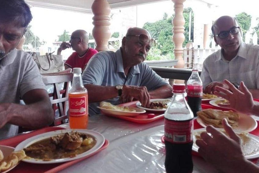 A group of people dining at an outdoor restaurant with tables covered in plastic, bottles of Coca-Cola, and plates of food. 5