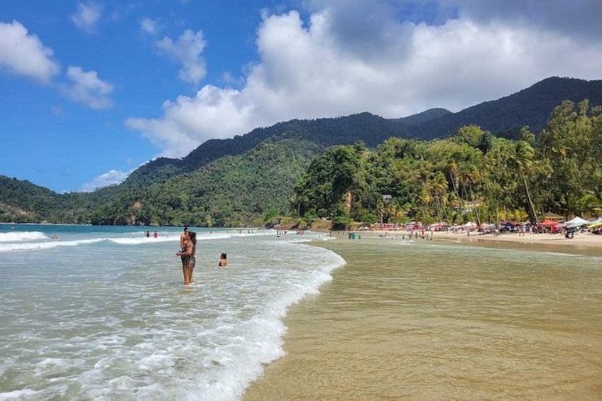 A beach with clear water, people swimming, and a forested mountain in the background. 3