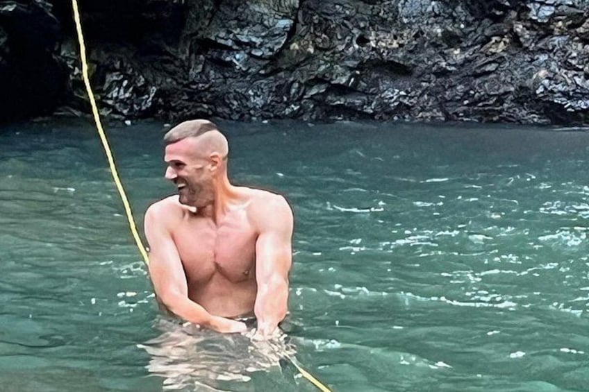 A man in a natural water body, possibly a river or lake, with rocky terrain in the background. 2