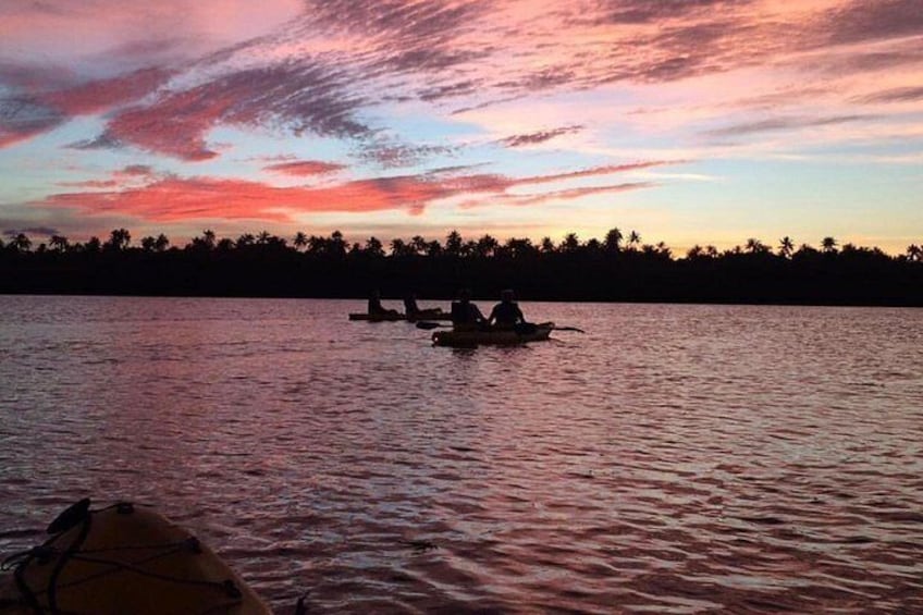 Un coucher de soleil sur une étendue d’eau, avec la silhouette d’une forêt et de deux bateaux. 2