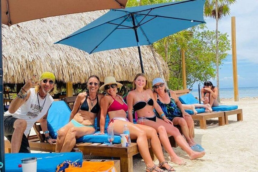 A group of people lounging on beach chairs under a thatched umbrella. 3