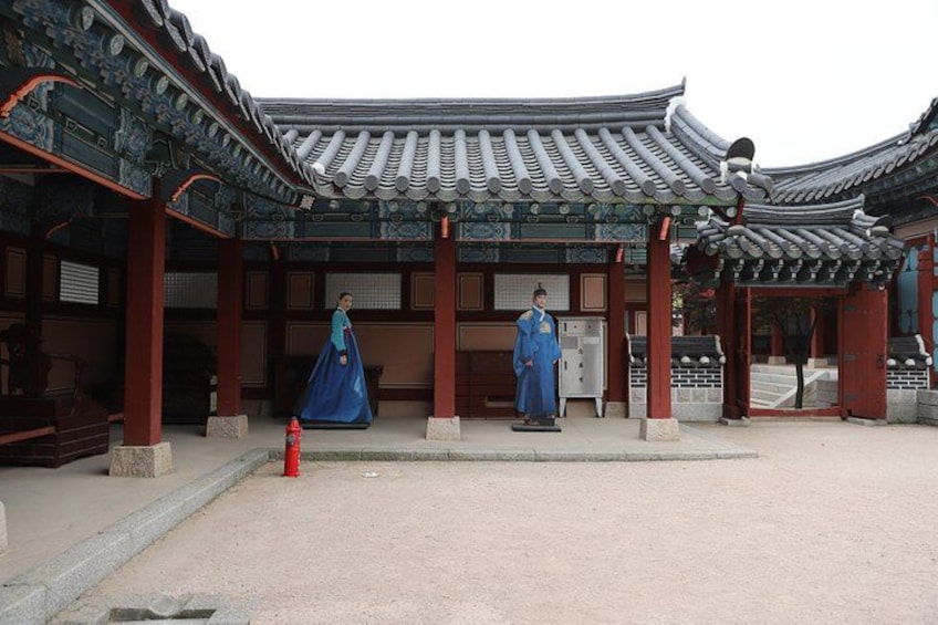 Un edificio coreano tradicional con arquitectura ornamentada, una estatua y una persona vestida con traje tradicional. 2