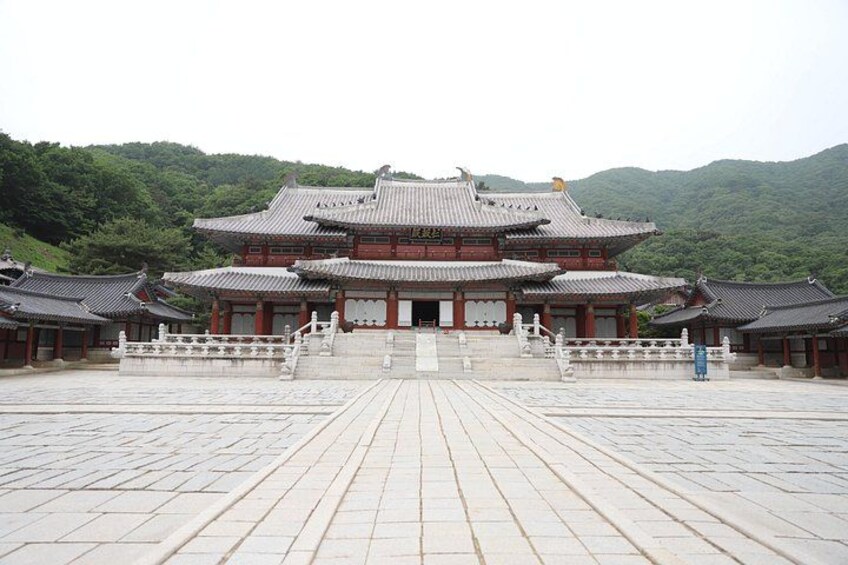Un palais coréen traditionnel doté d’une vaste cour, de toits couverts de tuiles rouges et grises, et surplombant un paysage montagneux. 2