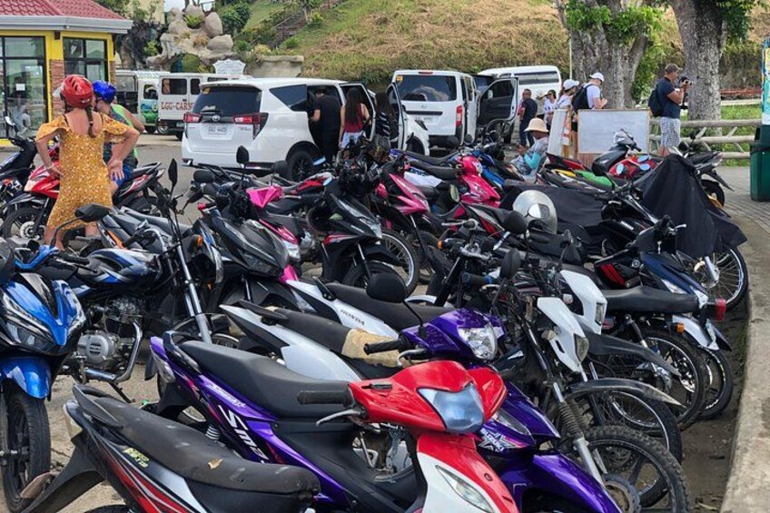 A row of motorcycles parked in a line, with people standing nearby. 2
