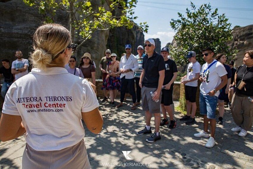 Un grupo de personas de pie al aire libre, algunas vestidas con camisetas que tienen impreso 'METEORA THRONES Travel Center'. 4