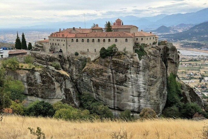 A historic building perched atop a rocky cliff, overlooking a valley. 3
