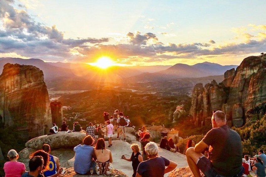 A group of people sitting on a rocky outcrop overlooking a valley with a sunset in the background. 5