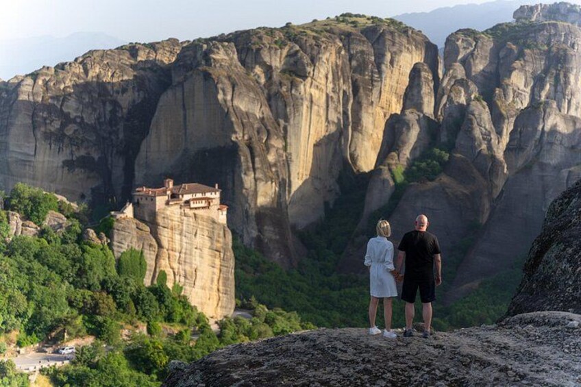 Un couple se tient sur un promontoire rocheux, d’où l’on aperçoit une falaise sur laquelle est perché un monastère. 3