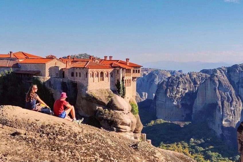 A historic building with red-tiled roofs, perched on a rocky cliff overlooking a deep valley. 3